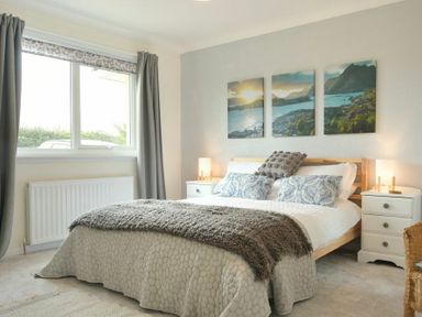 A bedroom with a bed bedside tables lamps and landscape paintings at Spuggies Rest in Embleton