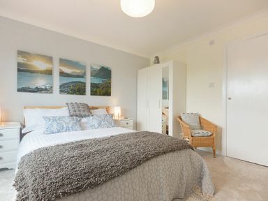 A bedroom with a bed bedside tables a chair wardrobe and landscape artwork on the wall at Spuggies Rest in Embleton