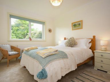 A bedroom with a bed covered with a blue blanket and towels beside a wooden chair and a window at Spuggies Rest in Embleton