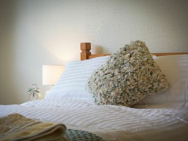 A bed with a wooden headboard a textured pillow a lamp and an alarm clock on a nightstand at Spuggies Rest in Embleton