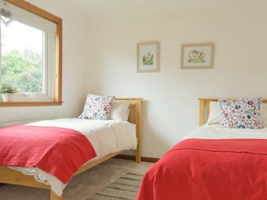 A bedroom with two single beds with red blankets and patterned pillows at Spuggies Rest in Embleton