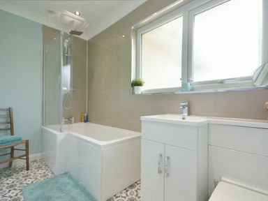 A bathroom with a bathtub shower combination a sink with cabinet a window and patterned floor tiles at Spuggies Rest in Embleton