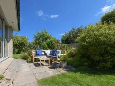 A patio with a wooden bench and table surrounded by plants and grass at Spuggies Rest in Embleton
