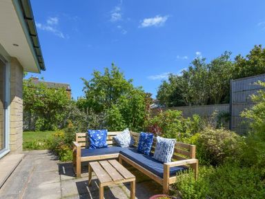 A garden patio with wooden bench seating and a small wooden table surrounded by greenery at Spuggies Rest in Embleton