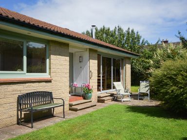 An outdoor patio area with a bench and two lawn chairs outside a house at Spuggies Rest in Embleton