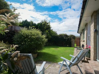 A garden with two chairs on a stone patio and a grassy lawn next to a house at Spuggies Rest in Embleton