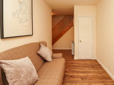 A room with a brown sofa with cushions a door wooden stairs and a framed picture of Winnie the Pooh at Stewart House in Wooler