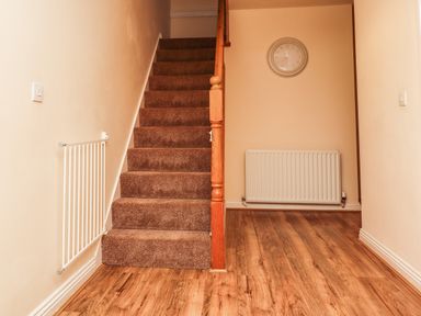 A hallway with wooden flooring a carpeted staircase a wall clock and two radiators at Stewart House in Wooler