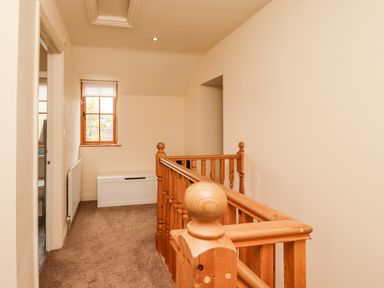 A hallway with wooden railing carpeted floor window and a white storage bench at Stewart House in Wooler