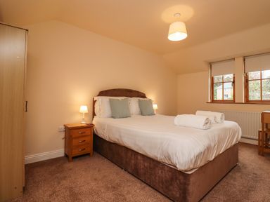 A bedroom with a double bed with pillows and rolled towels bedside tables with lamps a wardrobe and windows at Stewart House in Wooler