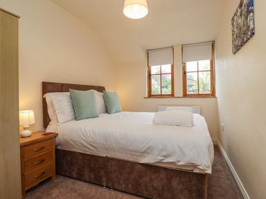 A bedroom with a double bed with pillows and folded towels near two windows at Stewart House in Wooler