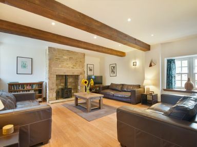 A living room with brown leather sofas a wooden coffee table with sunflowers and a stone fireplace at The Warren in Bamburgh