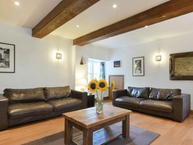 A living room with two brown leather sofas wooden beams on ceiling and a wooden coffee table with sunflowers at The Warren in Bamburgh