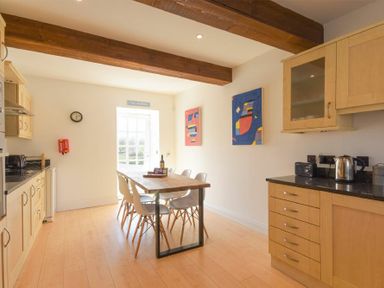 A kitchen with wooden beams wooden cabinets a dining table with chairs and colorful paintings on the wall at The Warren in Bamburgh