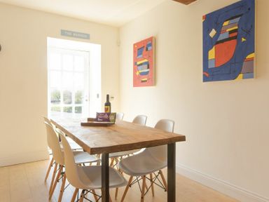 A dining room with a wooden table six white chairs and abstract paintings on the wall at The Warren in Bamburgh