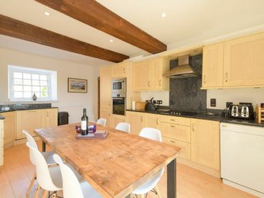 A kitchen with wooden cabinets a wooden dining table and white chairs at The Warren in Bamburgh