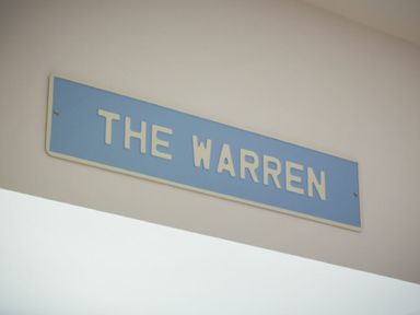 A blue rectangular sign with white text saying THE WARREN on a white wall at The Warren in Bamburgh