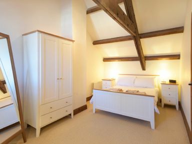 A bedroom with a white bed flanked by two bedside tables a white wardrobe and wooden ceiling beams at The Warren in Bamburgh