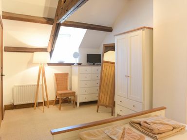 A bedroom with a bed, wardrobe, chest of drawers, chair, floor lamp, and full-length mirror at The Warren in Bamburgh