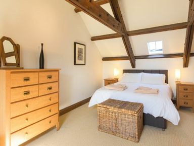 A bedroom with a bed cushions and blankets two bedside tables lamps and a wicker chest at The Warren in Bamburgh