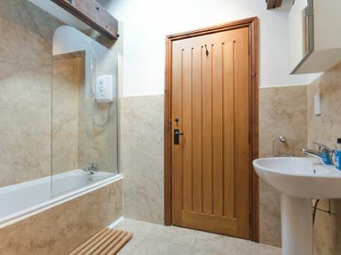 A bathroom with a bathtub shower combination wooden door and a pedestal sink at The Warren in Bamburgh