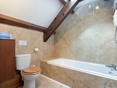A bathroom with a toilet with a wooden seat and a bathtub with a glass shower screen at The Warren in Bamburgh