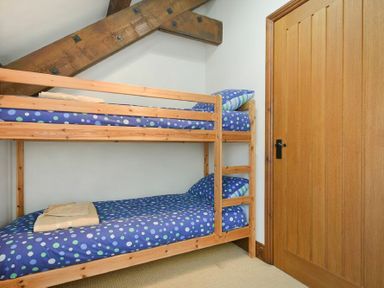A wooden bunk bed with blue polka dot bedding and folded towels in a room with wooden door and exposed wooden beam at The Warren in Bamburgh