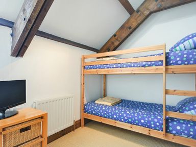 A bedroom with wooden bunk beds with blue polka dot bedding and a small TV on a wooden stand at The Warren in Bamburgh