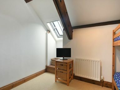 A small room with a skylight window a wooden side table with a monitor wicker baskets a radiator and part of a bunk bed at The Warren in Bamburgh