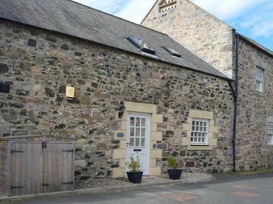 A stone exterior wall with a white door and window two potted plants and a wooden shed at The Warren in Bamburgh