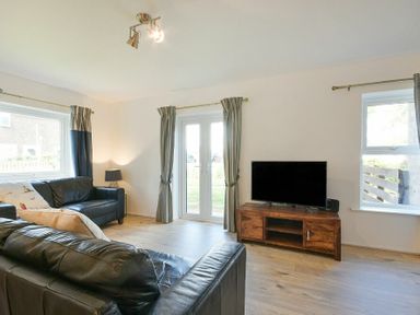 A living room with leather sofas a wooden TV stand and windows at Coastal Plaice in Beadnell