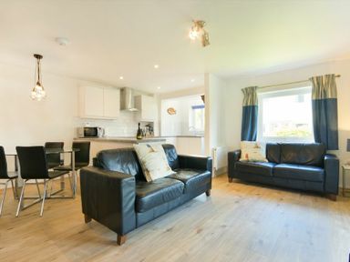 A living room with two black leather sofas and a dining table with black chairs in an open plan kitchen area at Coastal Plaice in Beadnell