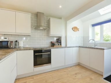 A kitchen with white cabinets a microwave oven a kettle and a window at Coastal Plaice in Beadnell
