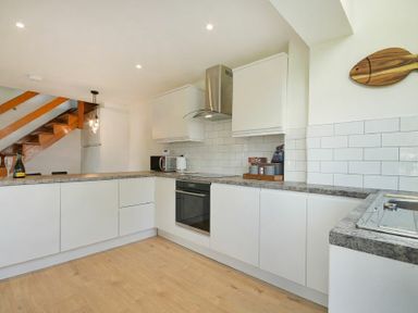 A kitchen with white cabinets a built in oven a microwave and a wooden staircase in the background at Coastal Plaice in Beadnell