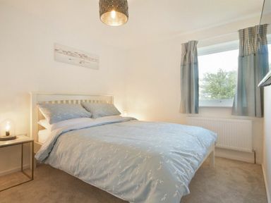 A bedroom with a double bed blue bedding curtains on window and bedside table with lamp at Coastal Plaice in Beadnell