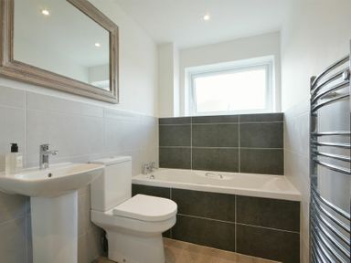 A bathroom with a sink a toilet a bathtub a mirror a window and a heated towel rail at Coastal Plaice in Beadnell
