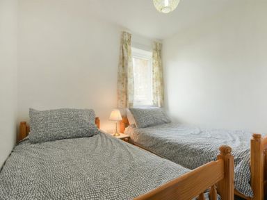A bedroom with two single beds with patterned bedding and a bedside table with a lamp at Coastal Plaice in Beadnell