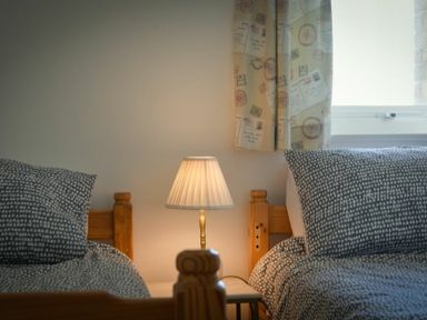 A bedroom with two wooden beds a lamp on a table and a window with patterned curtains at Coastal Plaice in Beadnell