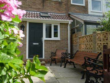A front yard with two benches and a black door on a brick house at Coastal Plaice in Beadnell