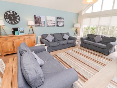 A living room with three grey sofas a striped rug wooden sideboard and large windows at The Wynd in Bamburgh