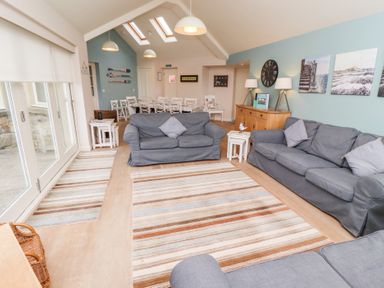 A living room with multiple grey sofas a dining table with chairs and wall decorations at The Wynd in Bamburgh