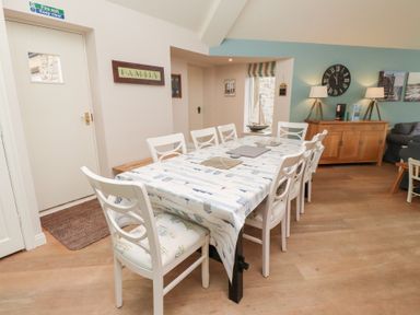 A dining area with a long table covered with a patterned tablecloth and white chairs at The Wynd in Bamburgh
