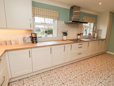A kitchen with white cabinets wooden countertops patterned tiled floor and two windows at The Wynd in Bamburgh