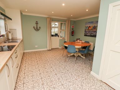 A kitchen with patterned floor tiles a round dining table with blue chairs and a door with curtains at The Wynd in Bamburgh