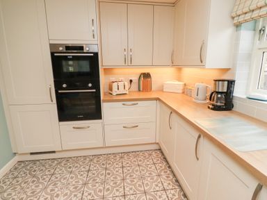 A kitchen with white cabinets a built-in oven a toaster a knife block a kettle and a coffee maker at The Wynd in Bamburgh