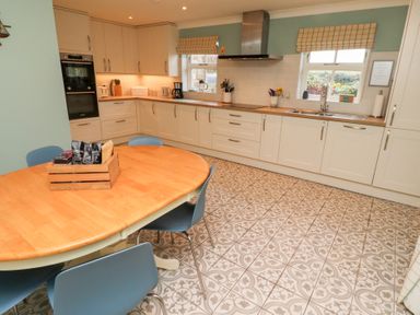 A kitchen with white cabinets wooden countertops a round wooden dining table with blue chairs and patterned tile floor at The Wynd in Bamburgh