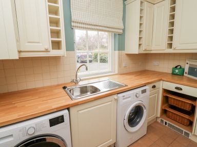 A kitchen with a washing machine dryer sink wooden countertop and window at The Wynd in Bamburgh