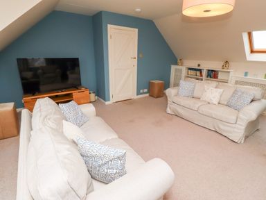 A living room with two beige sofas facing a television on a wooden stand and a bookshelf along the wall at The Wynd in Bamburgh