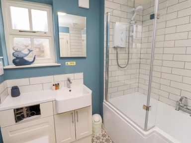 A bathroom with a bathtub shower combination a sink cabinet and a window with whale decorations at The Wynd in Bamburgh