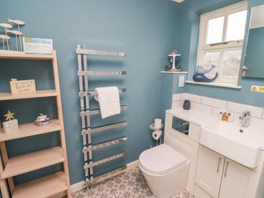 A bathroom with a toilet, sink, towel rack, window, and shelving unit at The Wynd in Bamburgh
